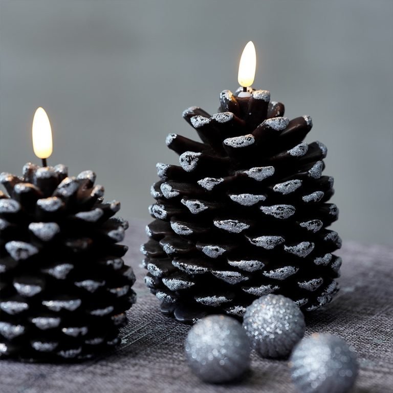 Two lit pinecone-shaped candles with glittery tips are placed on a surface next to three small glittery silver balls, creating Pinecone Magic: Transforming Your Home for a Festive Christmas.