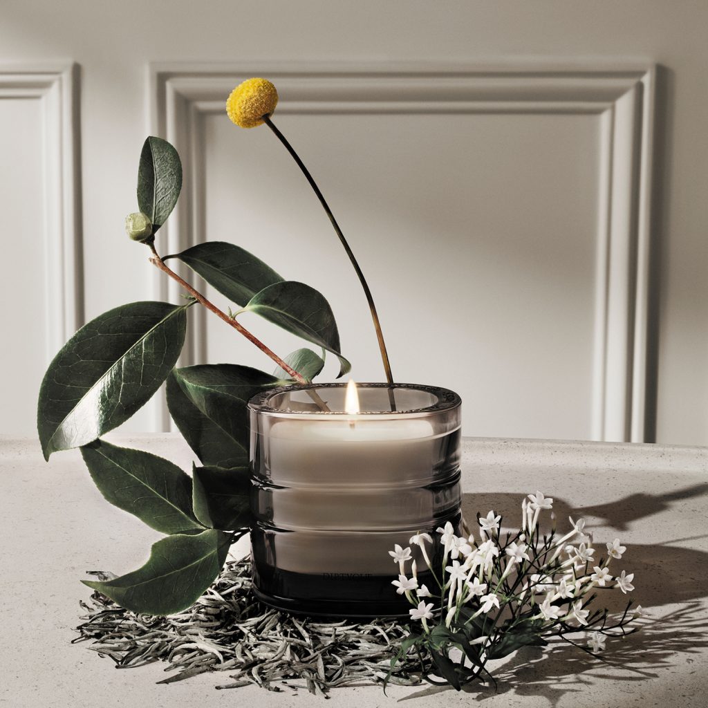 a Candle in a glass holder and some green leaves and a yellow flower on a table