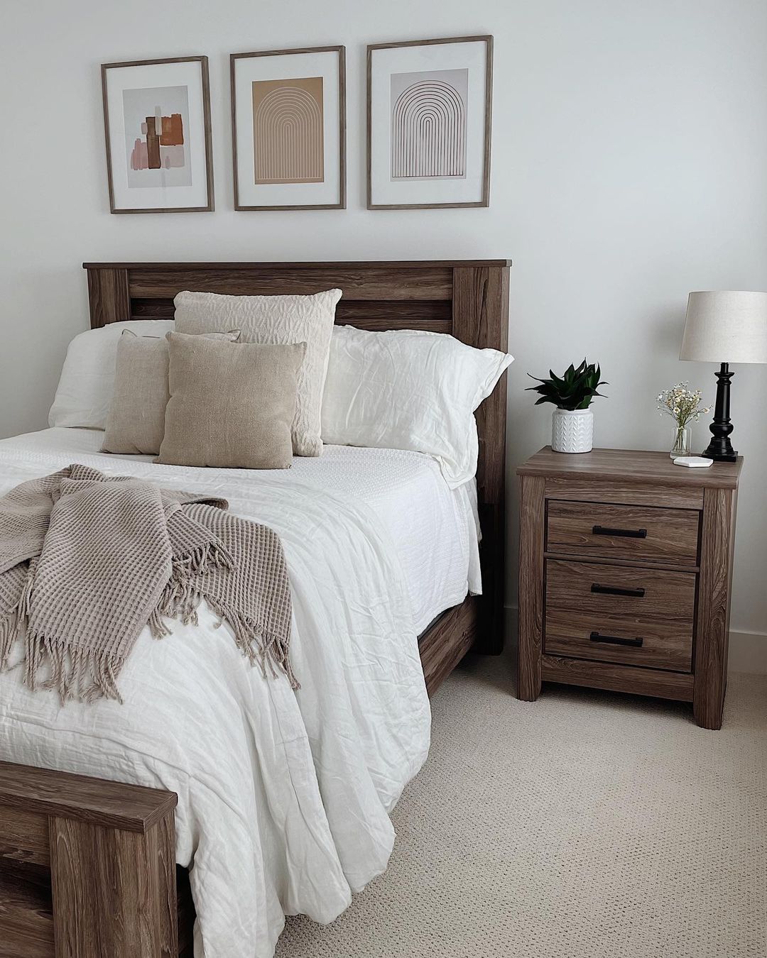a neutral-colored minimalist bedroom interior with wooden headboar, side table, and wall art