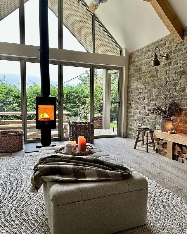 stone wall add a rustic touch to this living room with high ceiling and a large glazed end wall