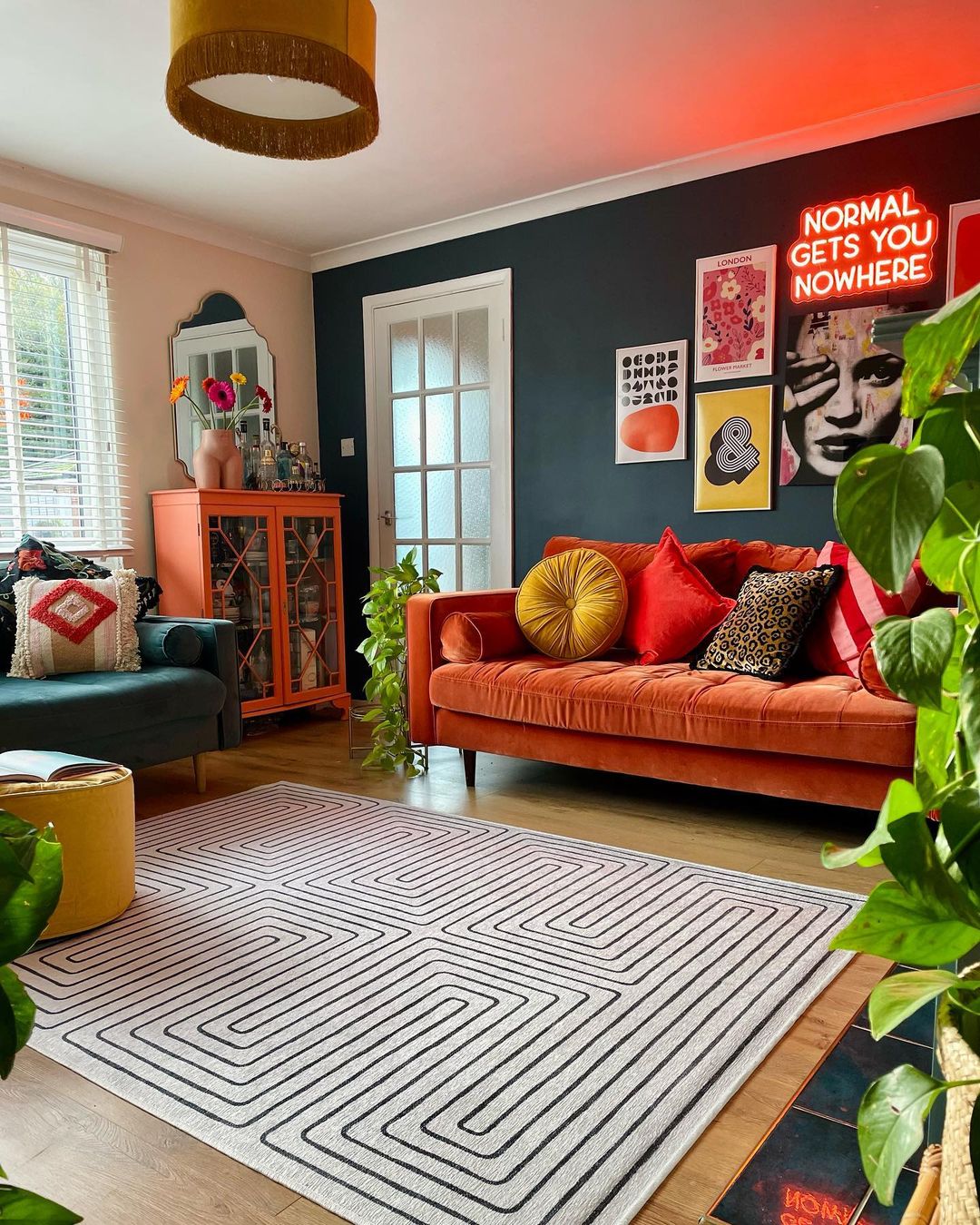 living room decorated with vibrant an orange couch and a green couch, dark green accent wall, colorful furniture, and geometric pattern floor rug