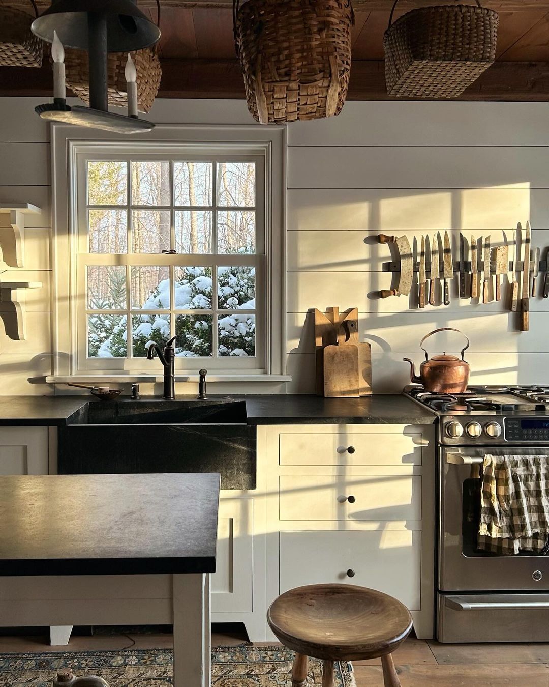 ceiling hanging baskets, a farmhouse sink, a stainless steel oven, and a neutral color scheme contribute to make this kitchen a blend of both cottage feel and modern clean line aesthetics.