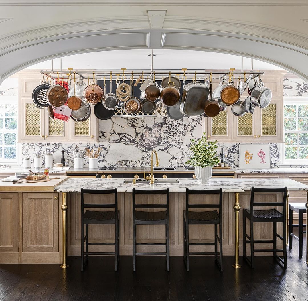 a central island and an overhang pot rack full of pots and pans to enhance both the functionality and aesthetic appeal to this modern kitchen