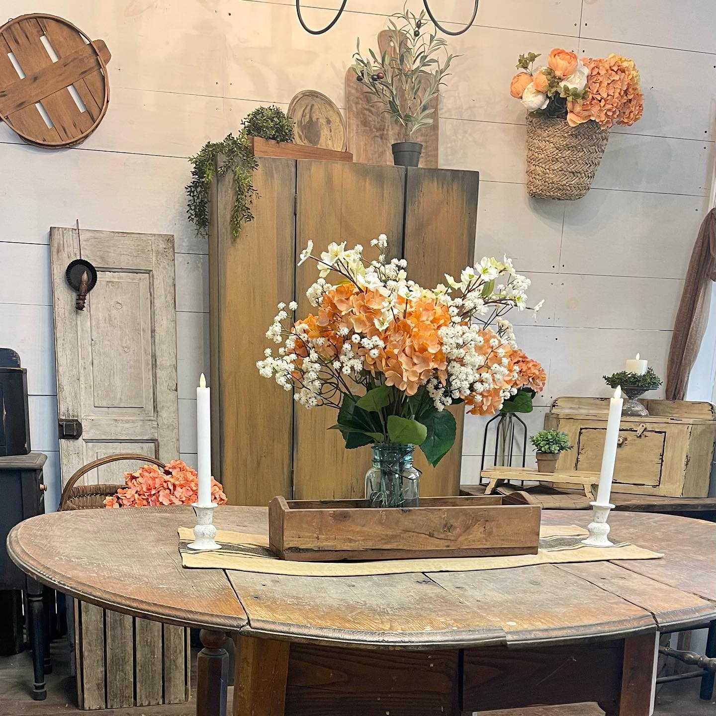 a wooden table styled with a centerpiece made of a wooden tray holding a Peach and white colored flowers and two candles with candleholders