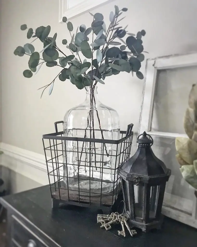 wire basket to hold a glass vase styled with green leaves with stem is an effortless way to update an entryway console table.