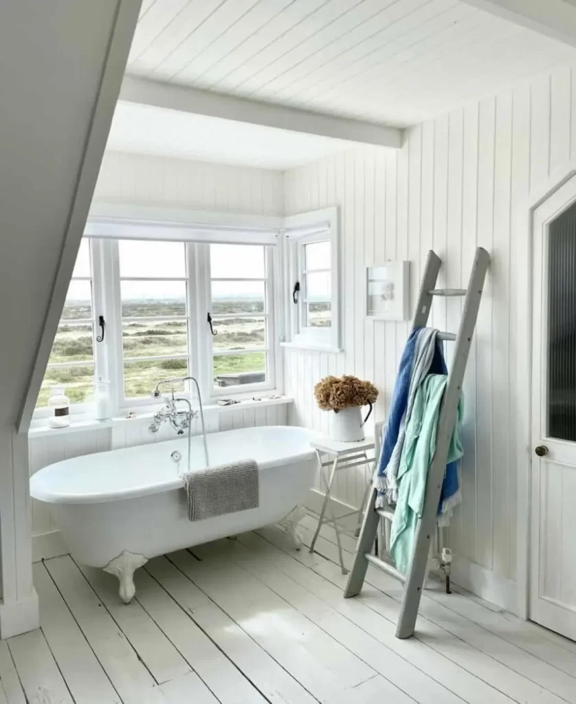 a beach style decorated bathroom can be as simple as all white wooden walls and floor, a freestanding white bathtub, beach-inspired wall art, and a wooden ladder as hanger.