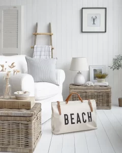 a living room in the beach decor style using white wooden shiplap wall and wooden floor styled with wicker ottoman-style side tables decorated with seashell accents and beach-inspired wall art add to the relaxed vibe of this interior.