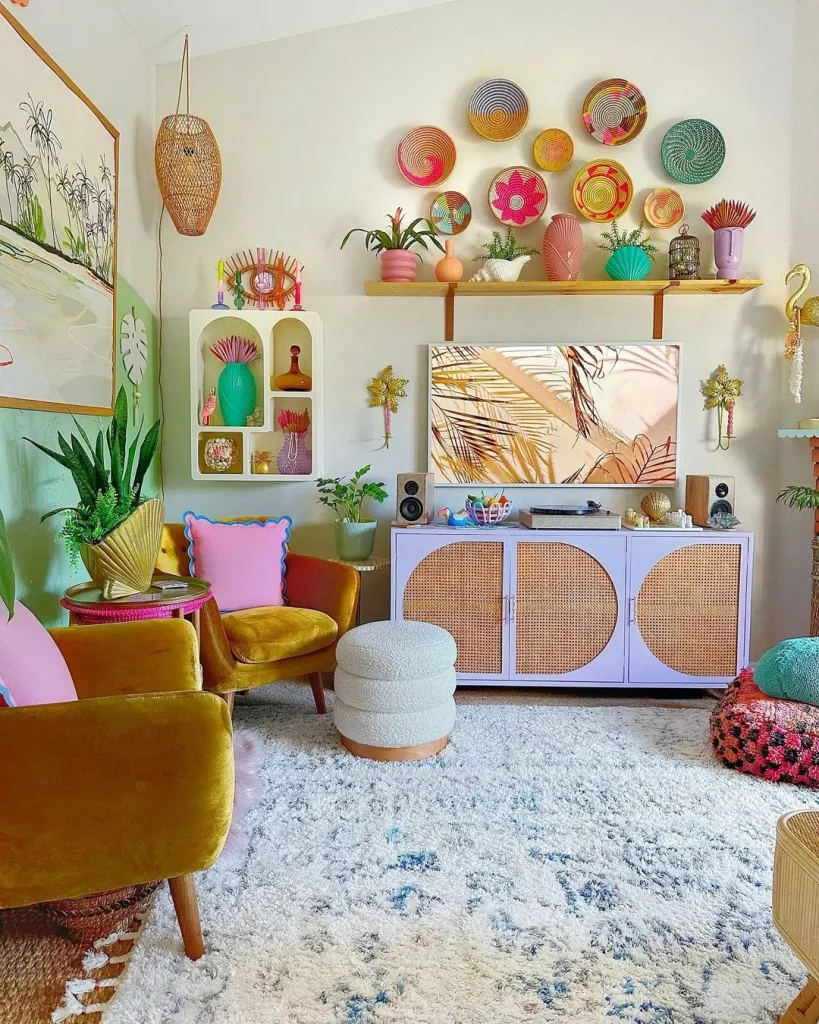 Colorful living room with mustard velvet chairs, pink and green accents, and woven baskets on the wall shows How To Achieve Funky Bohemian Living Room Décor. Plants, a patterned rug, pastel cabinet, and vibrant wall art complete the look.