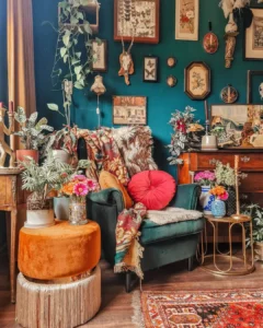 Eclectic living room featuring Maximalist Decor: Your Ultimate Guide to Bold Living Spaces—velvet armchair, colorful pillows, lush plants, a round orange ottoman, wall art, and decorative items set against a dark teal wall.