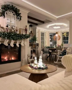 A cozy living room decorated for Christmas with stockings on the fireplace, a lit fire, festive ornaments, and a dining table set near large windows—one of 10 Cozy Christmas Living Room Ideas You’ll Love This Year.