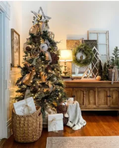 A decorated Christmas tree with lights and ribbon stands next to a wooden console table, with wrapped gifts in a basket and a wreath above—perfect inspiration for Rustic and Farmhouse Christmas Ideas: Simple Tips for Every Room.