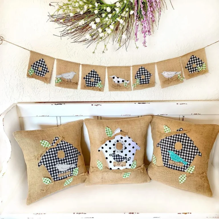 Summer farmhouse decor with burlap pillows and garland featuring buffalo check birdhouses and birds, displayed on a white bench with a floral wreath above