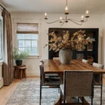 the earthy colors and plants selection in this dining room along with wooden furniture and modern minimalist lighting contribute to creating a beautiful organic modern space to dine in and connect with people
