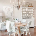 a french country-inspired dining room with a round wooden table and chairs complete with a candle-chandelier that add visual interest and warm glow to the room