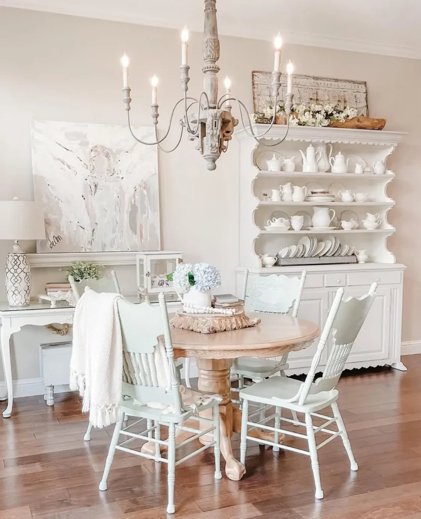 a french country-inspired dining room with a round wooden table and chairs complete with a candle-chandelier that add visual interest and warm glow to the room