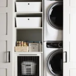 a beautiful laundry nook hidden behind sliding doors with a stacked washer and dryer on one side and open shelving on the other