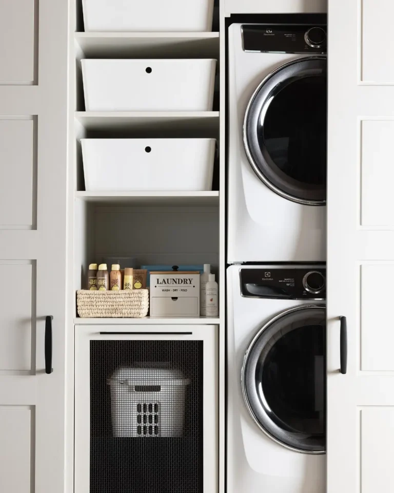 a beautiful laundry nook hidden behind sliding doors with a stacked washer and dryer on one side and open shelving on the other