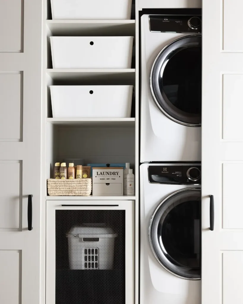 a beautiful laundry nook hidden behind sliding doors with a stacked washer and dryer on one side and open shelving on the other