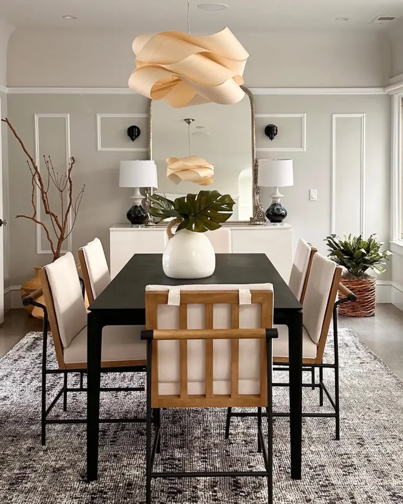 An Organic Modern Dining Room features a black table, six cushioned chairs, a large white vase with green leaves, a textured rug, and a sculptural ceiling light fixture.