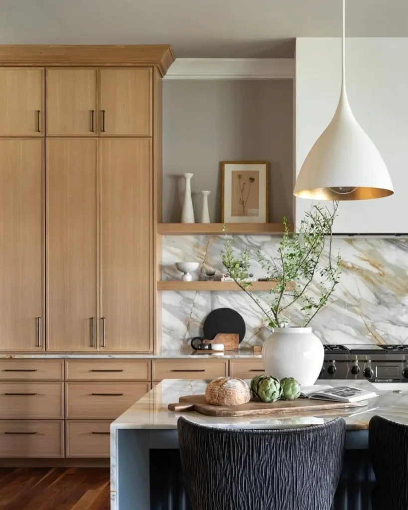 organic modern kitchen pendant lighting with clean minimalist lines accentuate the modern feel of this kitchen while displaying natural wood cabinets, a waterfall island, and even a potted green plant to elevate the natural look