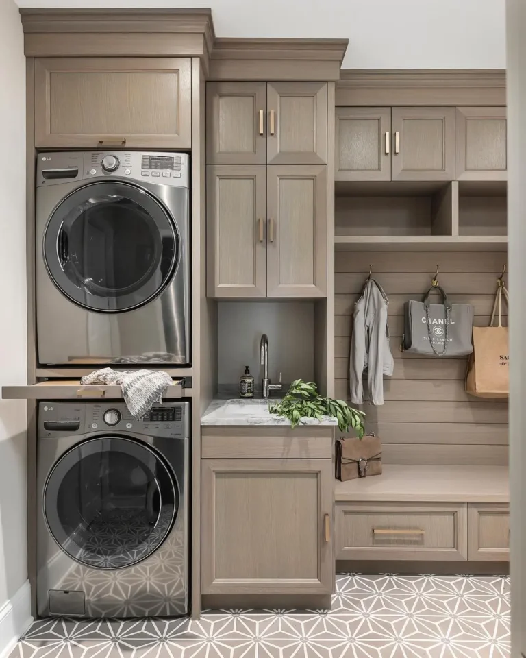 a stackable washer and dryer integrated into beautifully made cabinets in a mudroom with a small sink and alcove bench