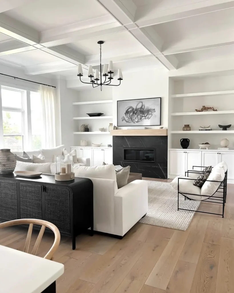 A modern living room with white walls, built-in shelves, a black fireplace, neutral furniture, and a large window letting in natural light creates an inviting organic modern atmosphere.