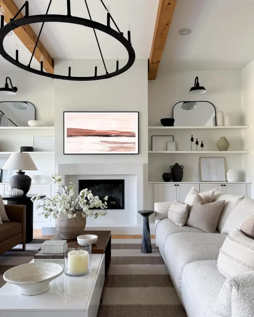 Modern organic living room with neutral tones, a large round chandelier, abstract art above a fireplace, built-in shelves, and a beige sofa with decorative pillows and coffee table.
