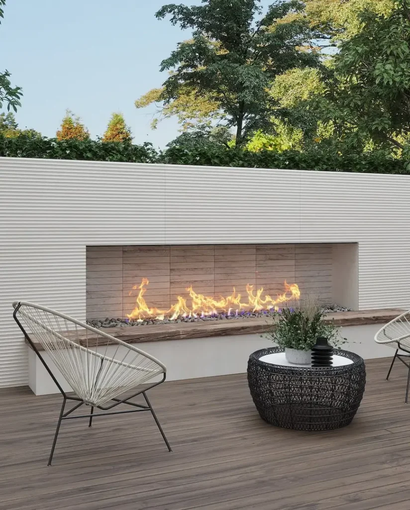 Modern organic patio with a long built-in fireplace, two wire-frame chairs, a round wicker table, and trees in the background.