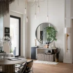 Entryway with stylish modern decor, featuring a round mirror, bench, plants, decorative objects, and pendant lights. Light wood floor, neutral walls, and a dining area with table and chairs complete the look.