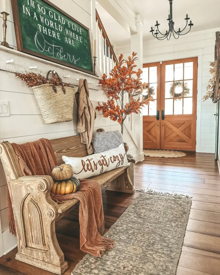 A farmhouse-style entryway with a wooden bench, autumn decorations, throw blankets, a chalkboard sign, and double wooden doors—your perfect inspiration from our farmhouse fall decor guide.