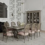 A formal dining room with a rectangular wooden table, eight pink cushioned chairs, a floral centerpiece, and a chandelier blends French country decor with other styles, complemented by a glass-front cabinet and decorative wall molding.