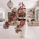A white vase with branches of red and brown leaves sits on a marble countertop in a modern, well-lit living room—perfect inspiration from a modern fall decor guide.