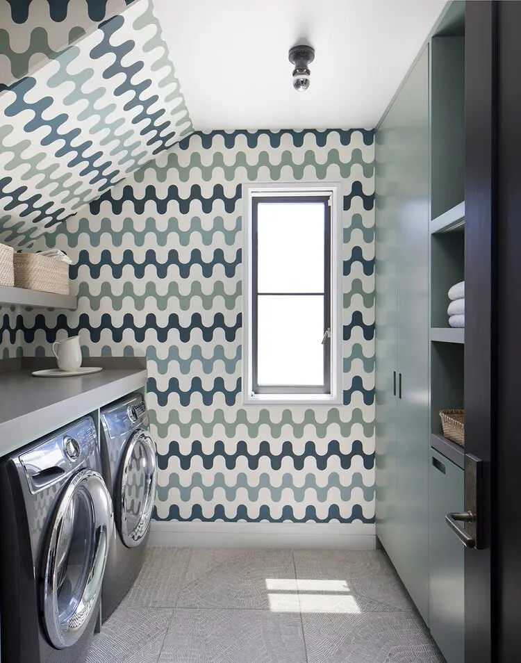 Modern laundry room with patterned faux tile wallpaper, a window, front-loading washer and dryer, open shelving, and neatly folded towels on the shelves.