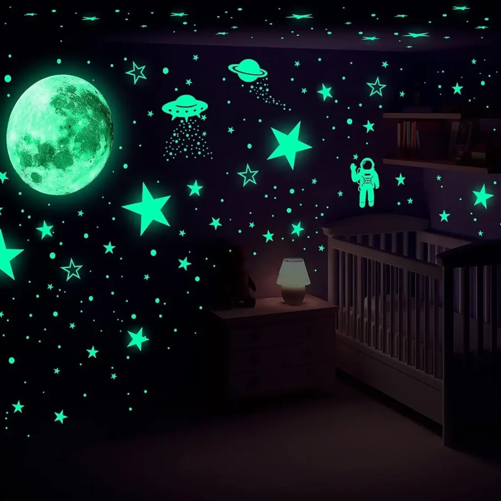 A dark nursery room with a crib, dresser, and glowing wall decals of planets, UFOs, an astronaut, a large moon, and enchanting glow-in-the-dark Christmas stars.