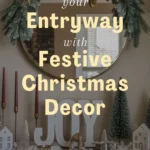 A decorated entryway with a pine garland and star wreath on a round mirror, “JOY” sign, candles, and miniature house figurines; text overlay about festive Christmas decor.