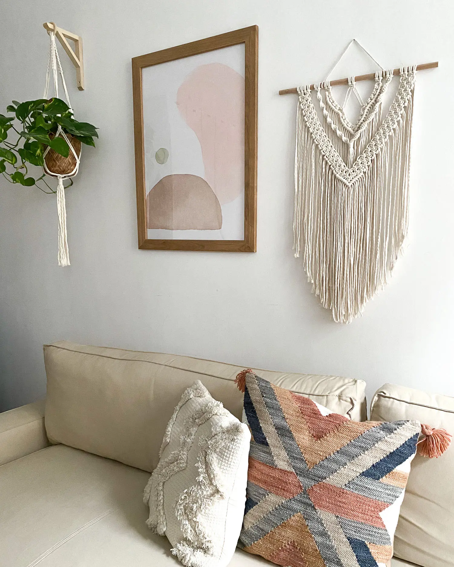 A white wall-hanging macrame styled on a living room wall above a sofa and next to a framed wall art to add a bohemian look to the space.