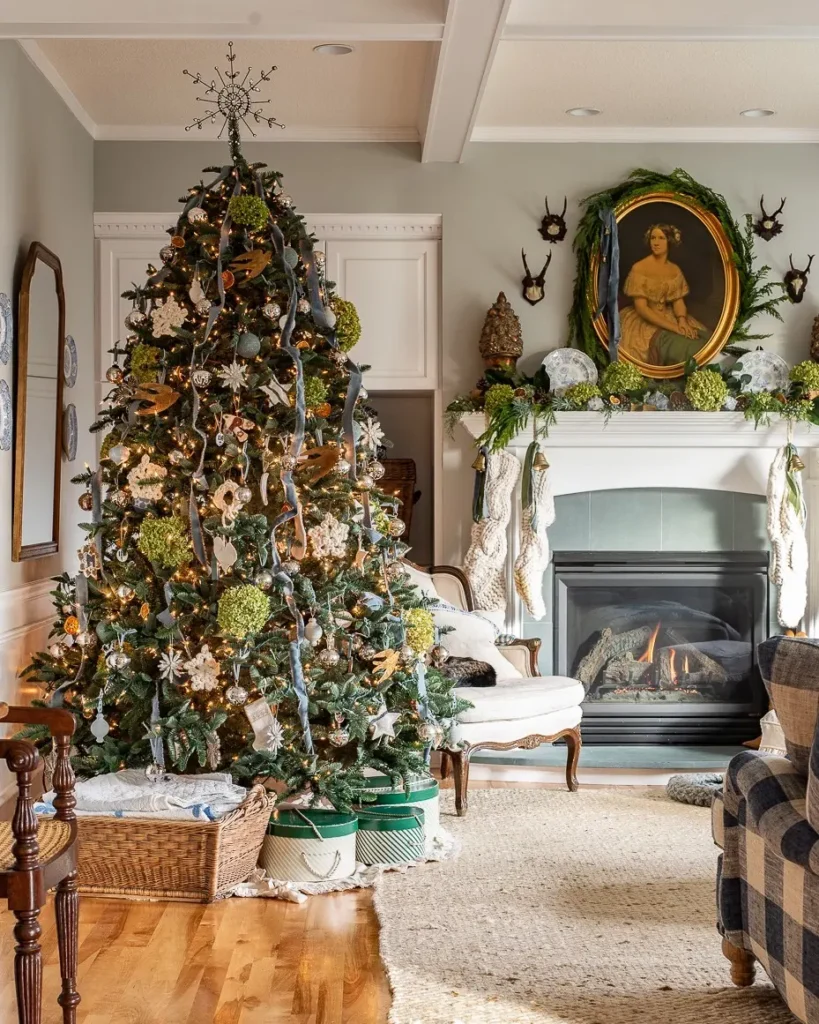 A decorated Christmas tree stands next to a fireplace in a cozy living room with wrapped gifts, a wicker basket, and framed art above the mantel.