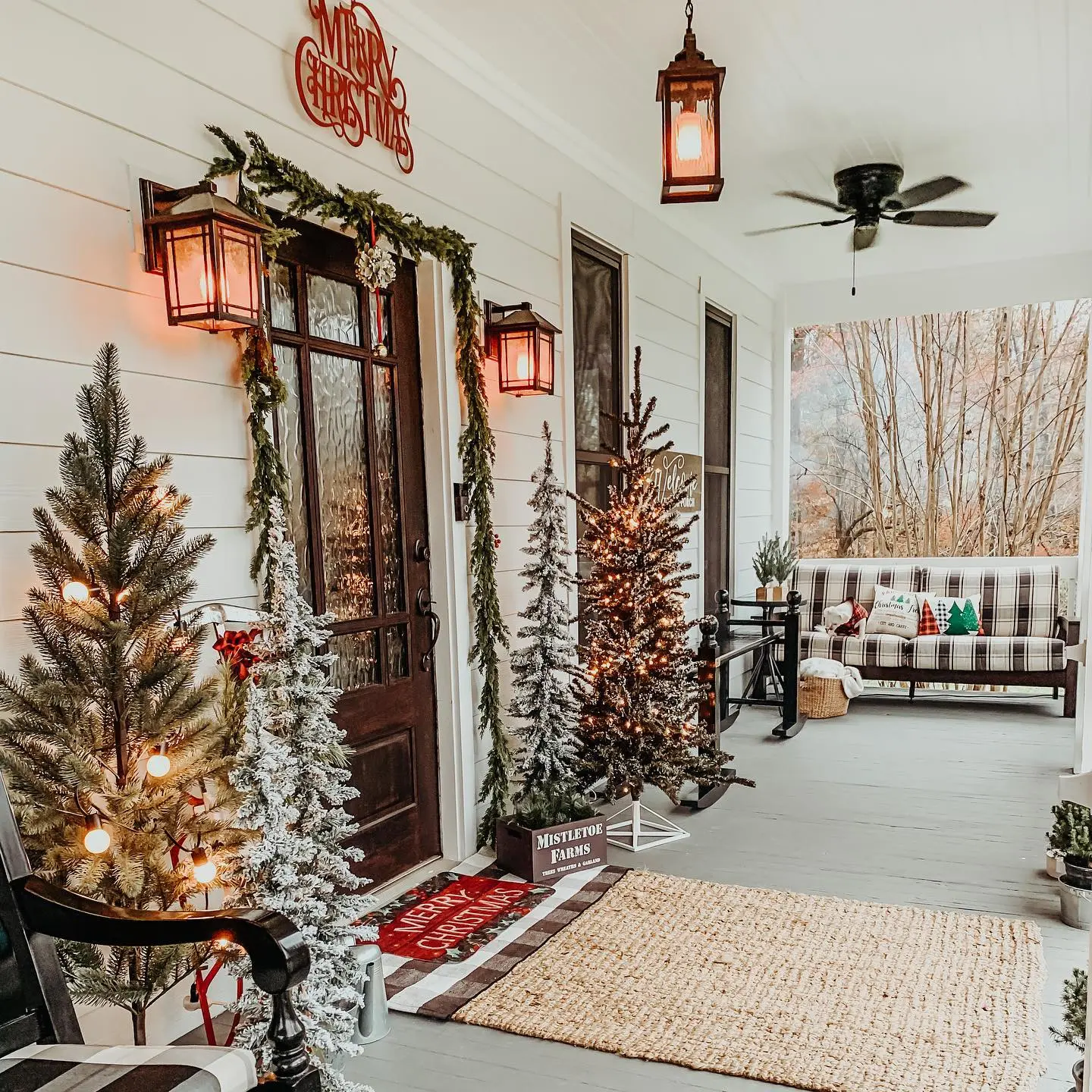 Christmas front porch decor ideas with frosted and natural Christmas trees, warm lantern lighting, plaid pillows, and a jute rug for a cozy farmhouse-inspired entryway.