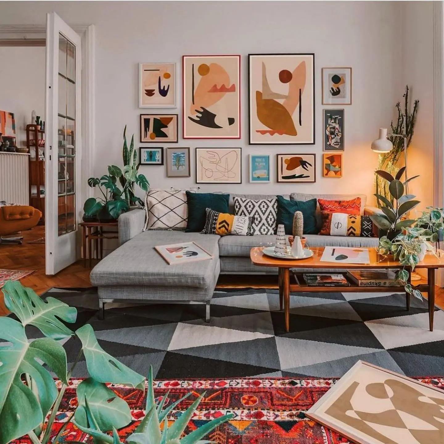 Boho living room with a gray sectional sofa, abstract art gallery wall, colorful throw pillows, layered rugs, and indoor plants adding cozy, eclectic charm.