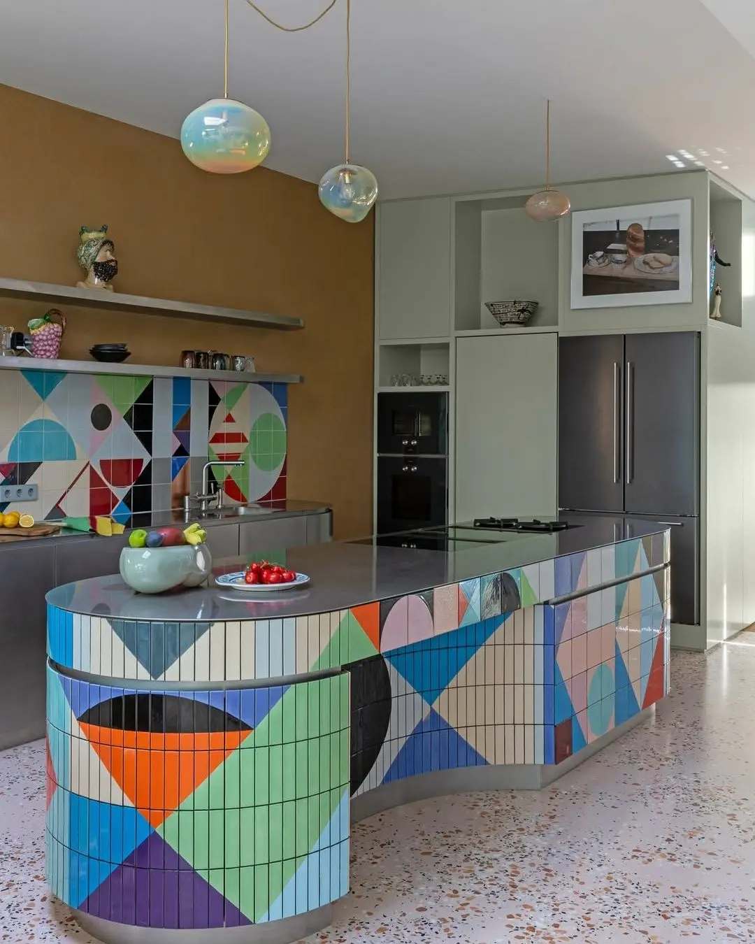 Modern kitchen with multicolored geometric tiles on the island and backsplash, gray countertops, minimalist cabinets, and three round pendant lights.