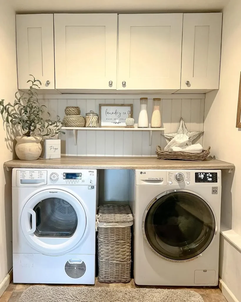 A laundry room with a dryer and washing machine beneath a countertop, a storage basket between appliances, decor items, and cabinets above the counter and on the shelf.