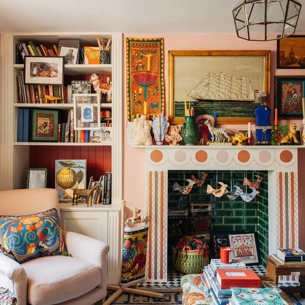 A colorful, maximalist fall living room features a decorated fireplace, shelves of books and art, a patterned armchair, and eclectic ornaments and framed artwork scattered throughout the vibrant space.