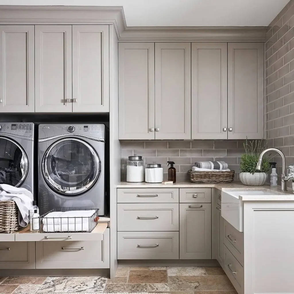 A modern laundry room with stacked washer and dryer, beige cabinets, a sink, countertop, and organized storage baskets and jars.