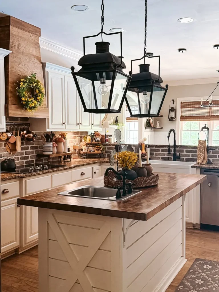 A farmhouse-style kitchen features white cabinets, brick backsplash, wooden countertops, and two large black lantern-style pendant lights over an island sink.