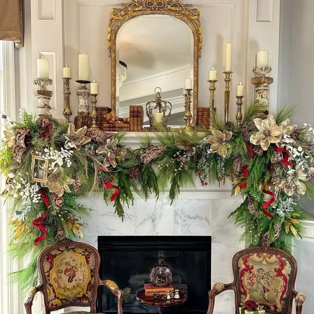 Elegant vintage Christmas mantel decorated with lush greenery, gold magnolia flowers, red ribbons, and antique candleholders beneath an ornate gold mirror, flanked by embroidered chairs for a classic old-world holiday look.