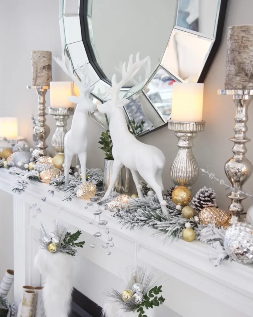 A Christmas mantel decorated with white reindeer figurines, gold and silver ornaments, pinecones, candles, and faux greenery, beneath a geometric mirror.