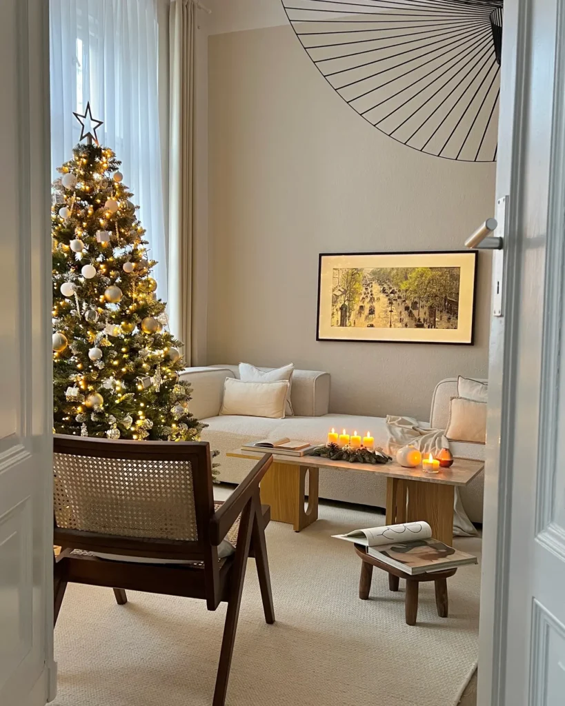 A cozy living room with a decorated Christmas tree, lit candles on a coffee table, modern furniture, and framed art on a beige wall—perfect for inspiring Christmas living room decor ideas for small spaces.