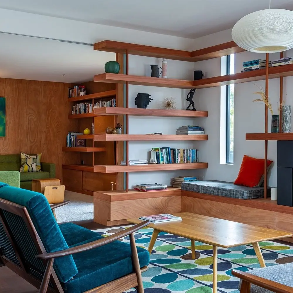 Modern living room with wood shelving, mid century modern furniture, green and blue accents, geometric rug, and a round white pendant light. Books and decor are neatly arranged on shelves.