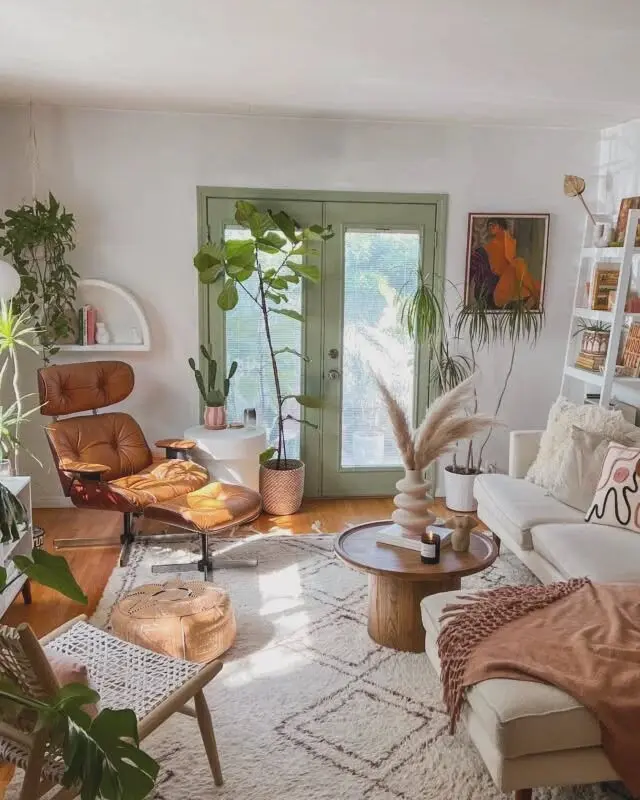 Bright living room with green double doors, plants, a white sofa, wooden coffee table, brown lounge chair, and wall art create an eclectic bohemian vibe in this cozy, sunlit space.