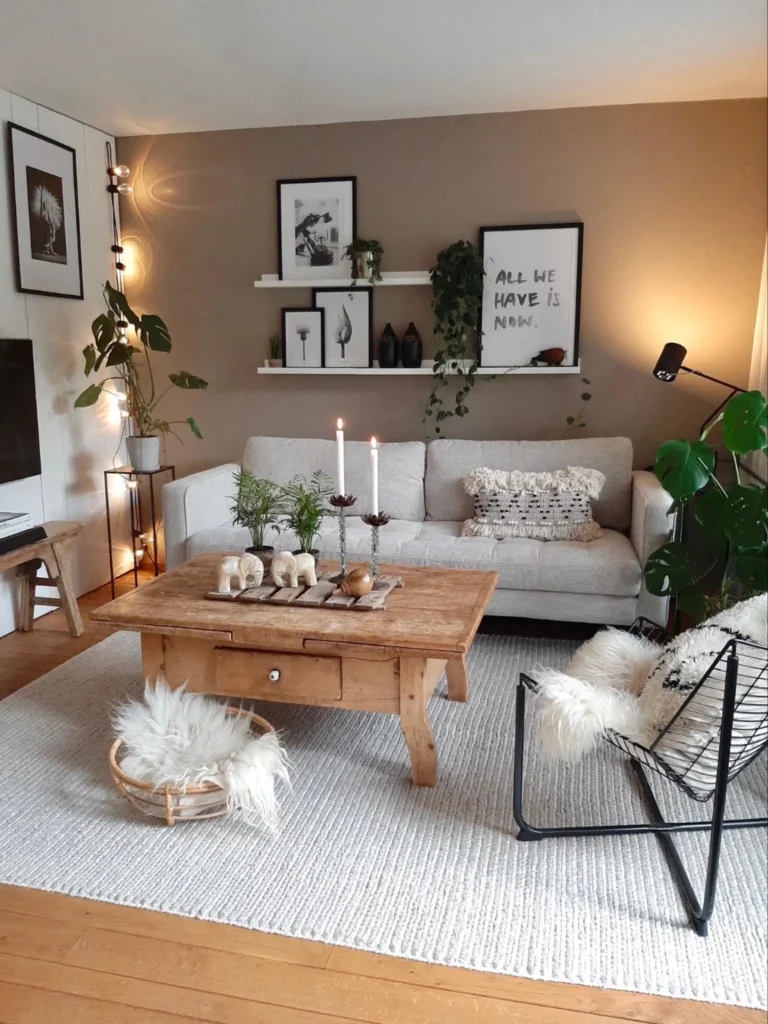 A modern living room with a beige sofa, wooden coffee table, black-framed chair, white rug, wall art, houseplants, soft ambient lighting, candles, and faux fur cushions for cozy winter decor.